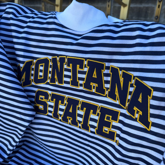 A close-up of a Montana State themed striped mocneck featuring navy and white horizontal stripes with 'MONTANA STATE' printed in navy and gold arched lettering across the chest.