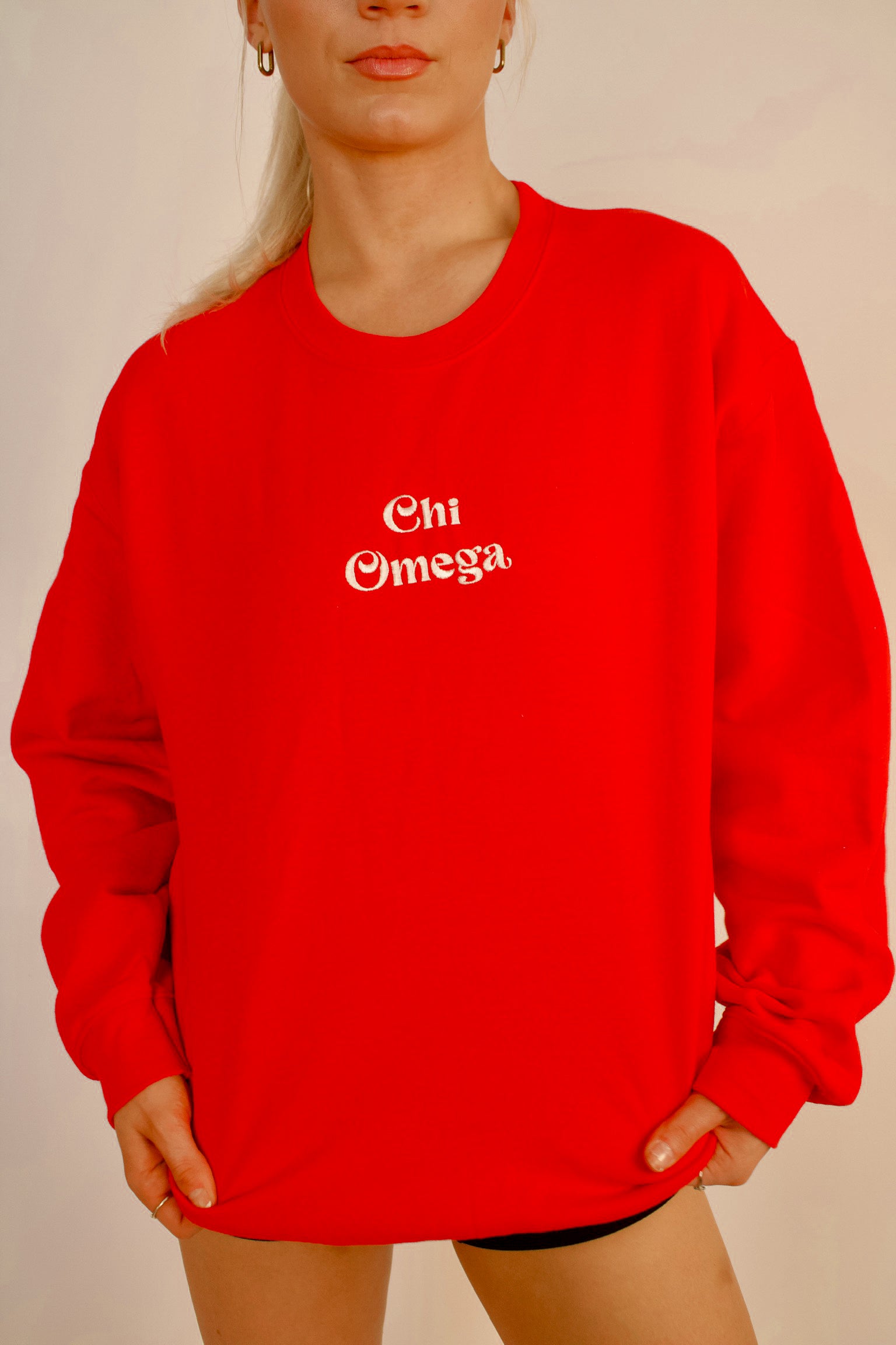 Person wearing a red sweatshirt with 'Chi Omega' text on a plain background